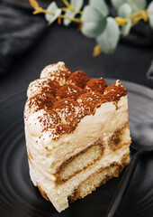 Traditional italian tiramisu cake on black plate