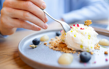 Sweet delicious dessert close-up with blueberries. A woman's hand with a spoon takes a dessert white cream. Breakfast in the cafe