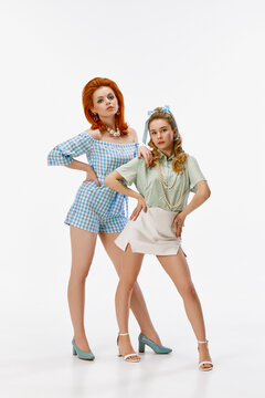 Full-length portrait of pretty young women with stylish hairdo and makeup, posing against white studio background. Concept of retro style, fashion, beauty, elegance, 60s, youth. Pin-up style