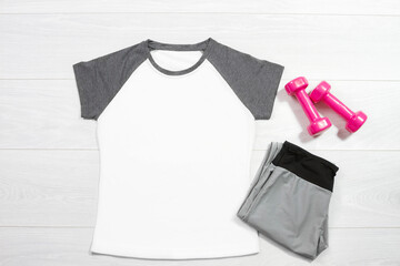 White female sport t shirt mock up flat lay on wooden background. Summer accessories. Sporty trousers, pink female dumbbells. Top front view t-shirt. Mockup tshirt. Template blank copy space
