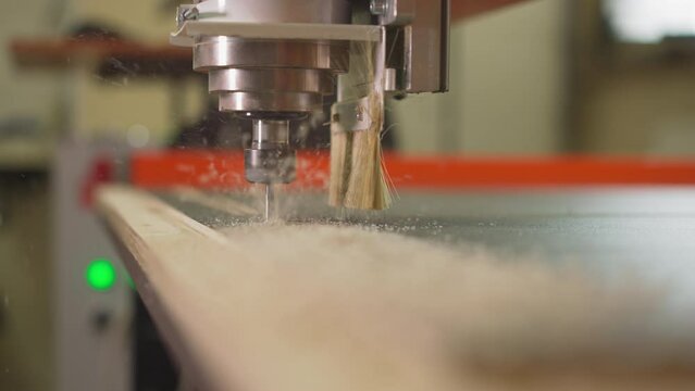 Automatic wood lathe machine with drill cuts out details of plywood sheet in carpentry workshop closeup. Small drill with connected brush creates sawdust at plant