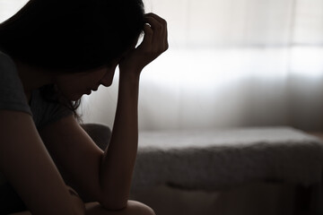 Depressed woman sitting alone on the bed with hands on head feel stress, sad and worried in the...