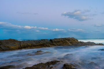 Long exposure water at the rocky coast against a blue sky