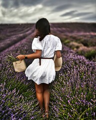 Vertical shot of a young woman in a short white dress walking in a lavender field