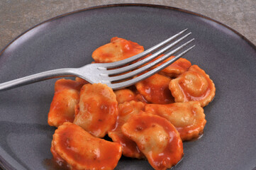 Assiette de ravioli sauce tomate avec une fourchette en gros plan