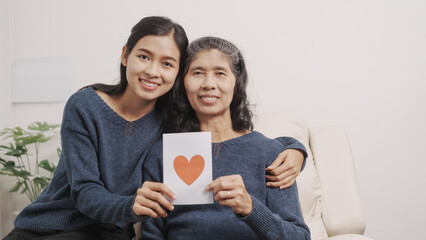 Greeting card, Mother's day concept, young adult female daughter congratulate excited asian elderly mother at sofa with birthday anniversary, two generations family photo, real people.