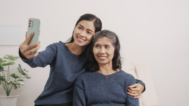 Shopping on mobile, Mother's day concept, young adult female daughter congratulate excited asian elderly mother at sofa with birthday anniversary, two generations family photo, real people.