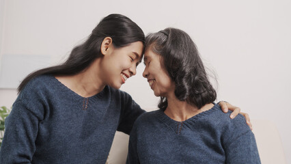 Hugging, kiss, love, Mother's day concept, young adult female daughter congratulate excited asian elderly mother at sofa with birthday anniversary, two generations family photo, real people.