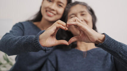 Hands heart shape, Mother's day concept, young adult female daughter congratulate excited asian elderly mother at sofa with birthday anniversary, two generations family photo, real people.