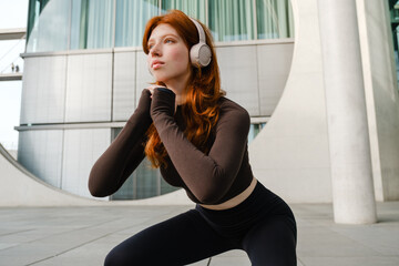 Obraz premium Young girl listening music with headphones while doing squats outdoors