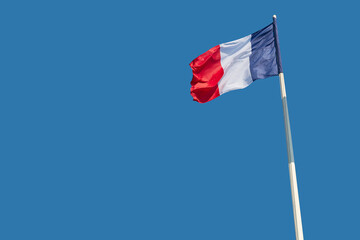 The national flags of France flutter against a blue sky.