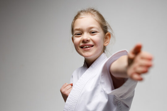 Smiling girl makes a punch on a white background, karate training.