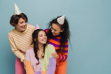 Three cheerful girls smiling while posing isolated over blue background