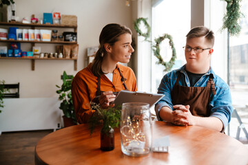Female with clipboard training man with down syndrome to work in cafe while sitting at table