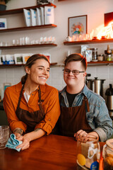 Man with down syndrome and his female colleague smiling while standing at counter in coffee shop