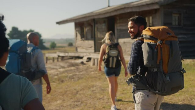 Rear view of group of friends with backpacks hiking in countryside together - shot in slow motion 