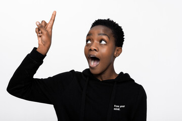 Portrait shot of pretty american dark skinned woman with short hair opening mouth white teeth showing something nice to friend pointing at up upwards standing over white background in studio.