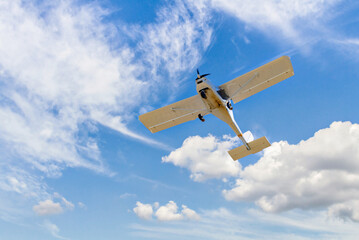 Single engine ultralight plane flying in the blue sky with white clouds