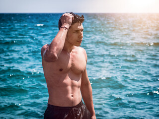 Athletic young man standing in ocean water, shirtless, looking away