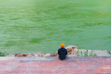 An Indian man in a turban meditates on the banks of a river. A Sikh sits on the banks of the Ganges.