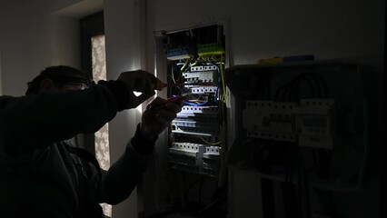 Man electrician installing solar panel system using headlamp. Close up technician in gloves making electrical wiring inverter and electric box. Concept of alternative and renewable energy.
