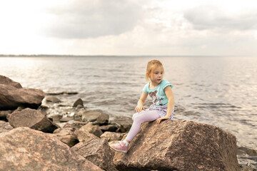 Fototapeta na wymiar A little girl is sitting on the rocks by the sea. Gulf of Finland. Summertime