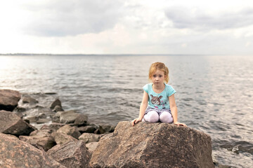 Fototapeta na wymiar A little girl is sitting on the rocks by the sea. Gulf of Finland. Summertime