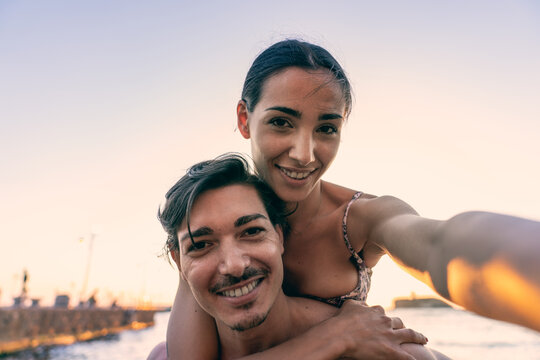 lifestyle photoshoot of young helthy beautiful caucasian couple, active boy and girl, dating at the beach - Man and woman lovers having fun in holidays taking selfies near the ocean in a sunny day