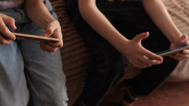 school-age children sitting on the couch use gadgets play mobile games on smartphones. children's attachment to gadgets. children's leisure time with phones