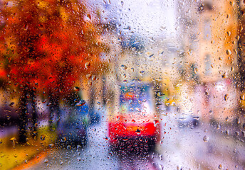 View through a glass window with raindrops on city streets with cars in the rain, bokeh of colorful city lights, night street scene. Focus on raindrops on glass