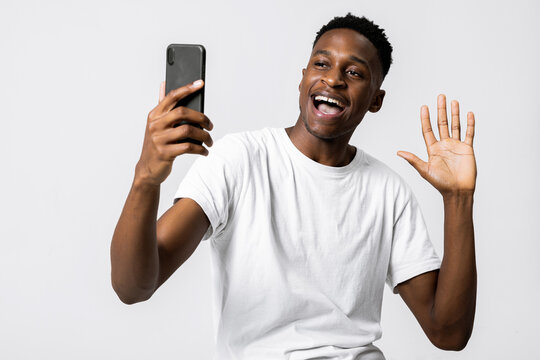 Handsome african american black man holding new modern last series smartphone in hands smiling having video conference with family taking picture having live strean on social media waving at camera.