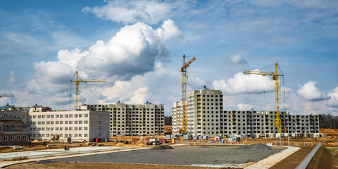  tower cranes working on construction with white fluffy curly rolling clouds as background