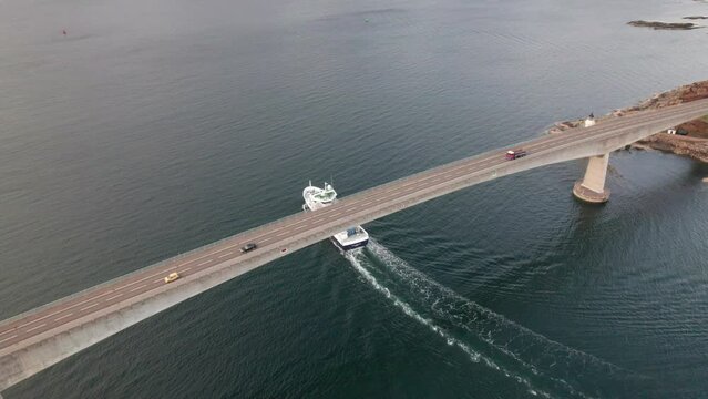 Boat going under the Kyle bridge while cars are going over the bridge into Isle of Skye, Scotland. Drone tracking shot.