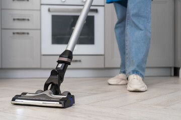 Close-up of a woman holding a vertical vacuum cleaner in her hands while cleaning in a modern kitchen. Employee of a cleaning company or a housewife cleans the house.