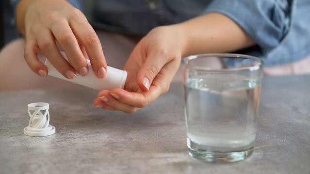 Female hands open jar of medicine and drop effervescent pill into glass water. Take pills, drugs, medicament, vitamins. Antipyretic and pain reliever