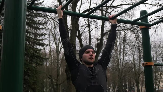 a guy performs a pull-up exercise on a horizontal bar on a sports field on the street, a man does sports, slow motion