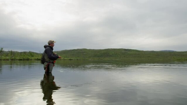 Wide static side view of young man fly fishing in still lake in Sweden