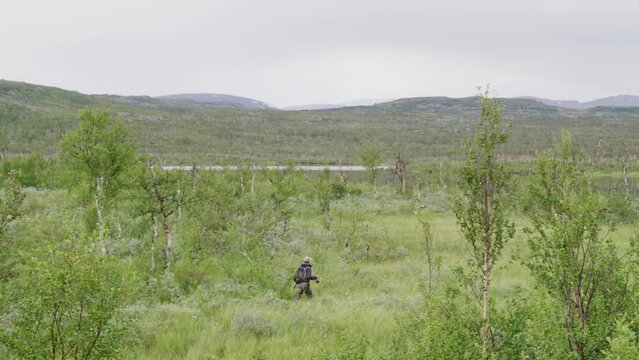 Wide view of man with fishing gear walking in green Swedish landscape
