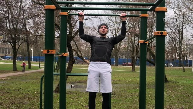 a guy performs a pull-up exercise on a horizontal bar on a sports field on the street, a man does sports, slow motion