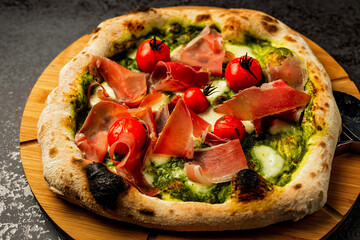 Pizza with prosciutto meat, cherry tomatoes, pesto and cheese served on a wooden board, close-up