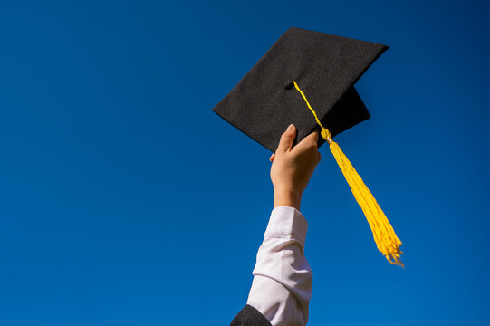 Close-up of a woman's hand with a graduation cap against the blue sky. 