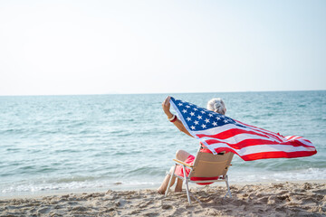 Mature woman holding US flag enjoying time at the beach.