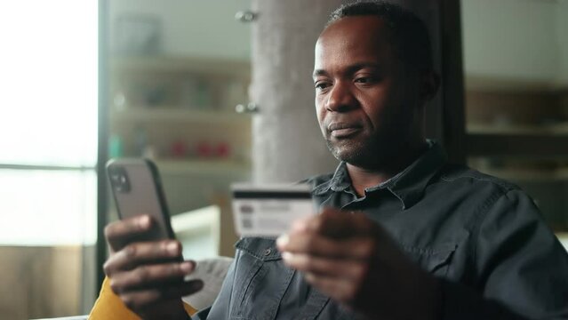 Portrait of mature african american man paying with credit card on smartphone cellphone at home Happy customer doing payments online shopping in internet store and receiving cashback Easy pay concept