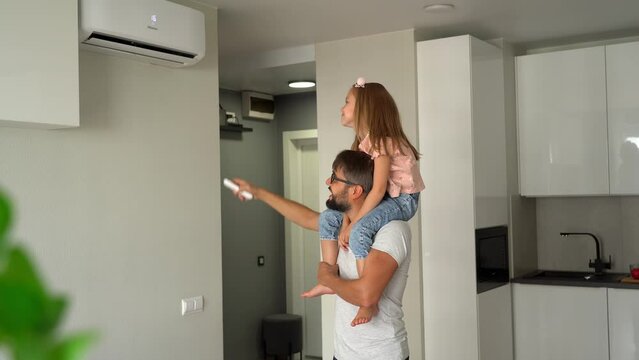 Father with little daughter on shoulders turn on air conditioner using remote control. Happy family adjust comfortable temperature of cooler system