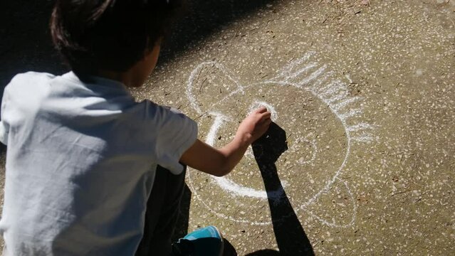 Happy kid on sidewalk draw with happy face. Boy with chalk in her hands on back door of the school draws on the asphalt. Children art. Happy boy draw a happy face on the sidewalk with colored chalk.