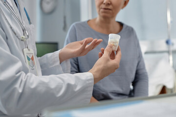 Close-up of doctor holding bottle with pills prescribing them to patient for treatment while they...