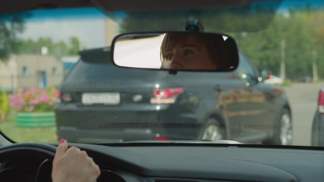Concerned female driver looks in car rear-view mirror to see road condition on back. Woman sits in automobile waiting for green traffic light to drive closeup