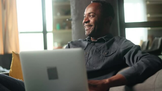 Portrait of mature african american man relaxing at home or working online on laptop computer looking at screen while his family or friend take photo indoors Smiling male posing for picture indoors