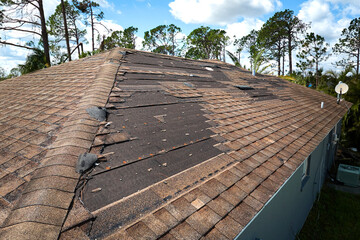 Damaged house roof with missing shingles after hurricane Ian in Florida. Consequences of natural disaster © bilanol
