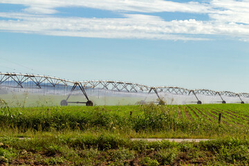 Máquina de irrigação molhando a plantação que está crescendo, em um dia claro com algumas nuvens no céu.